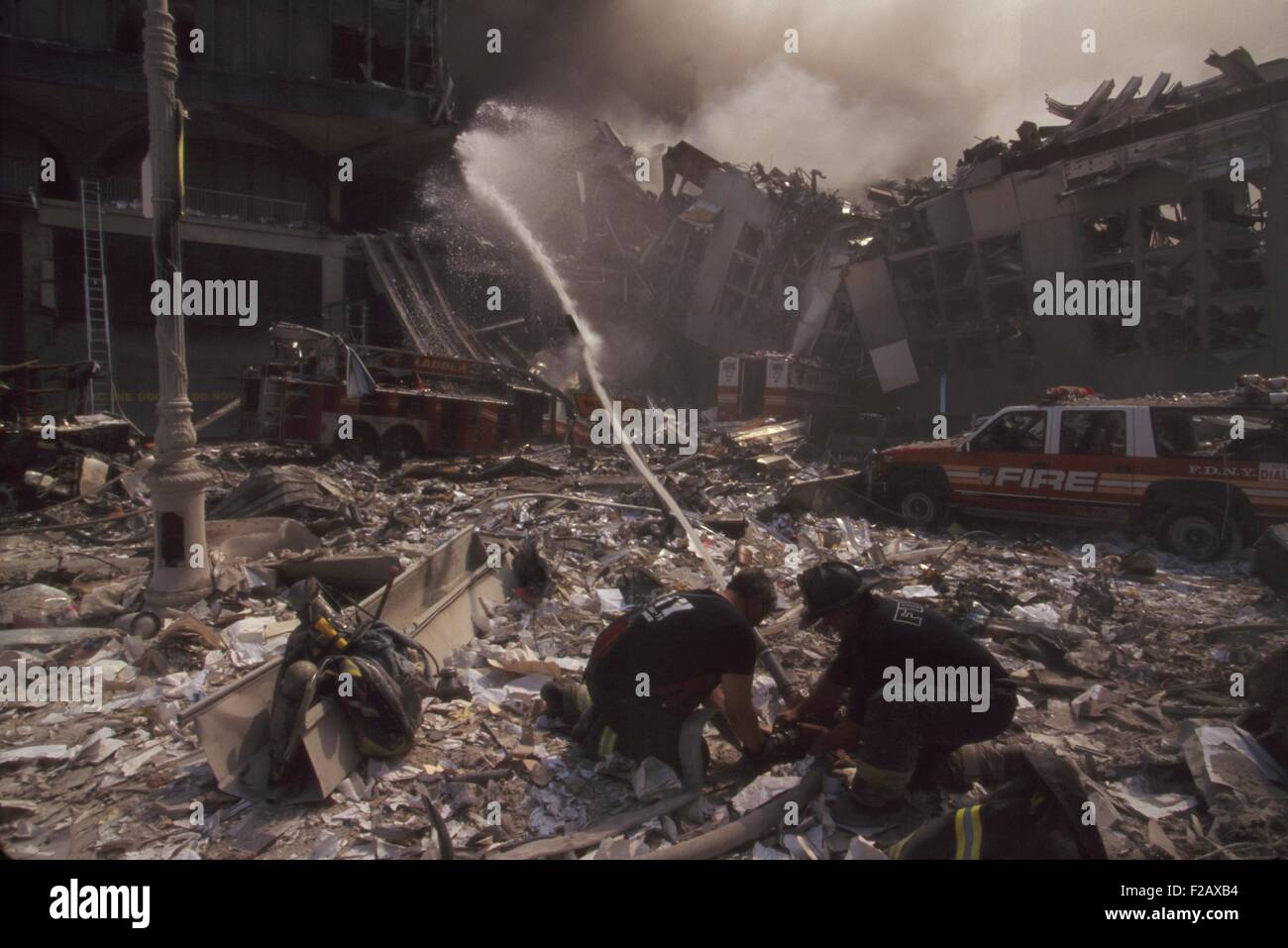 Fire fighters set up a hose amid smoking rubble following September 11th terrorist attack on World Trade Center. At left is still standing WTC 6. At right is the destroyed North pedestrian bridge over West Side Highway (West St.). The water stream is toward the burning pile of the collapsed WTC1 (North Tower). New York City, Sept. 11, 2001. (BSLOC 2015 2 48) Stock Photo