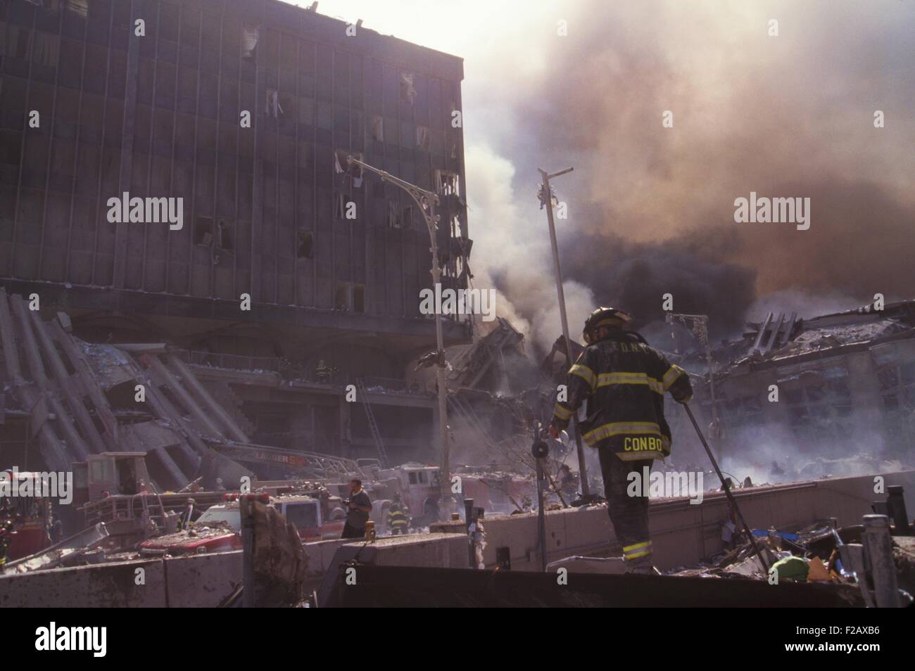 Fire fighters amid smoking rubble following September 11th terrorist attack on World Trade Center. Photo shows the still standing WTC 6 and the destroyed North pedestrian bridge over West Side Highway (West St.). In photo upper right is the smoke from the burning pile of the collapsed WTC 1 (North Tower). New York City, Sept. 11, 2001. (BSLOC 2015 2 46) Stock Photo