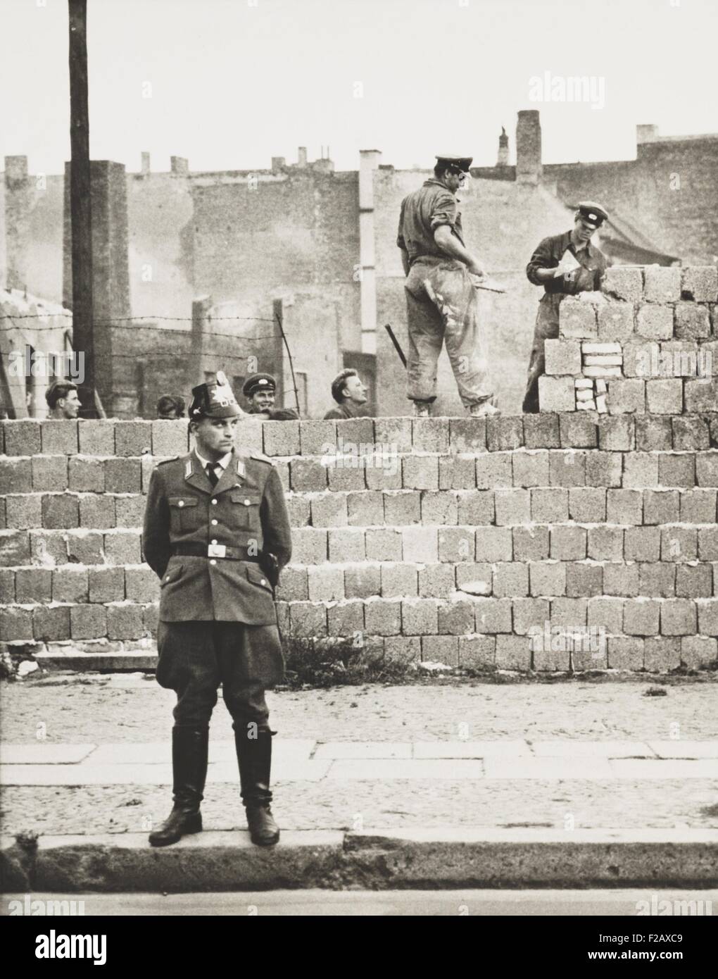West Berlin policeman stands before the concrete block wall dividing East and West Berlin. Along Bernauer Strasse, East Berlin workmen add blocks to increase height of the barrier. Oct. 11, 1961. (BSLOC 2015 2 265) Stock Photo