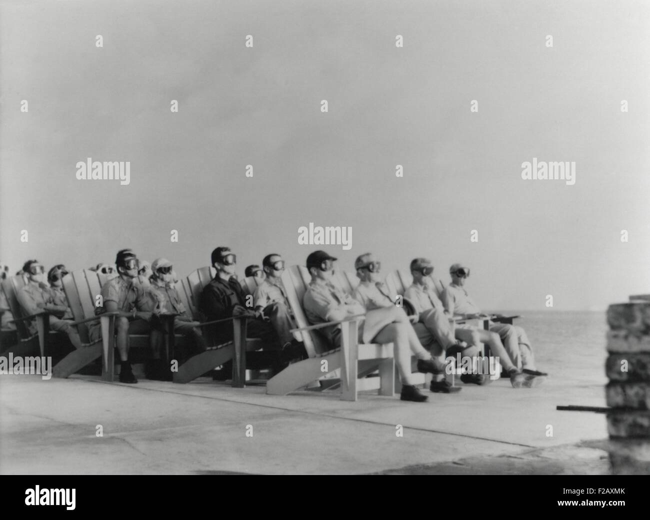VIPs view the DOG shot, an 81 kiloton atomic detonation wearing safety goggles. They are sitting on Adirondack chair of the Officers Beach Club patio on Enewetak Island. The blast wave arrived at the location of the VIPs some 45 seconds after the initially silent flash. April 7, 1951. It was first test in a series, Operation Greenhouse, that tested principles leading to developing thermonuclear weapons (hydrogen bombs). (BSLOC 2015 2 16) Stock Photo