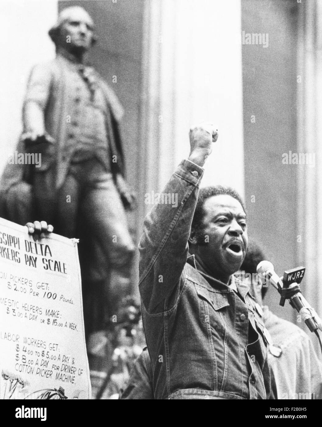 Rev. Ralph Abernathy speaks with a clenched fist on Wall Street on April 5, 1971. 4000 protestors marched in the Financial District demanding a guaranteed annual income of $6500. At left is a portion of a sign listing the poverty level wages of workers in the Mississippi Delta. In the background is a statue of George Washington at Federal Hall. (CSU 2015 9 1114) Stock Photo