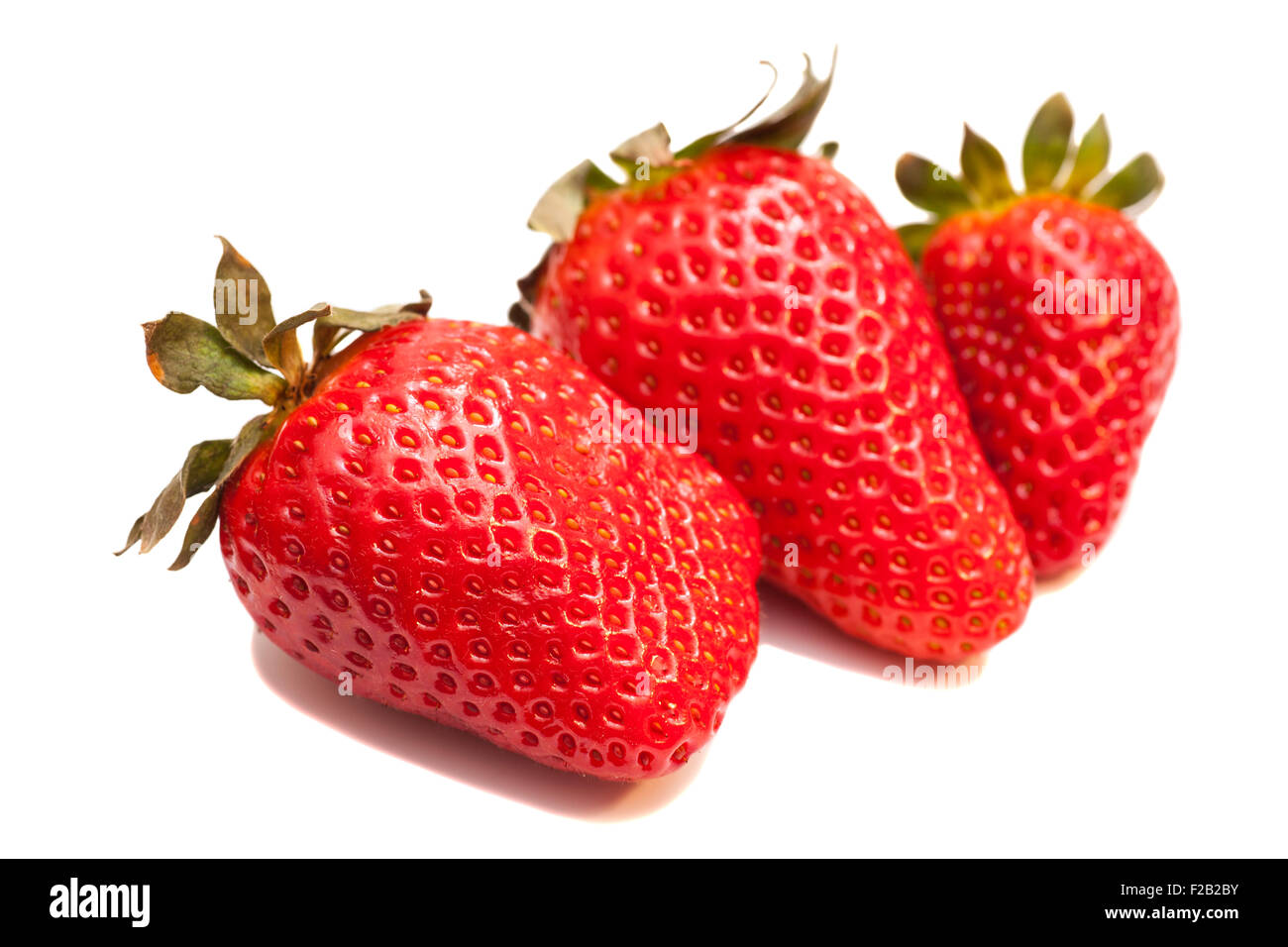 Three ripe strawberries with leaves on white background Stock Photo - Alamy