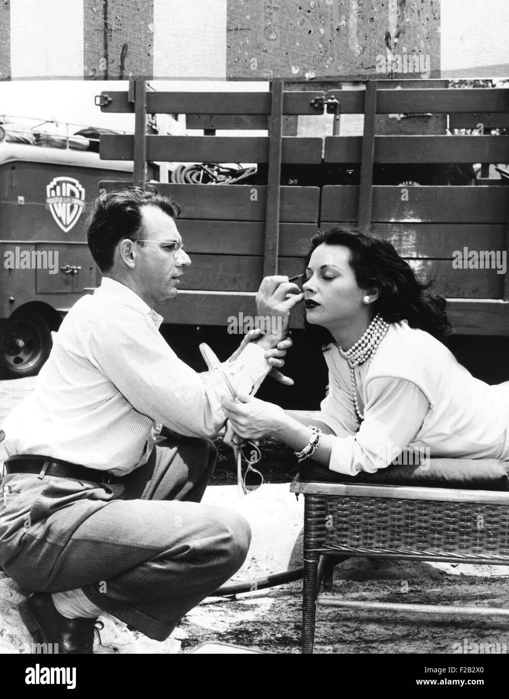 Makeup artist Ben Nye applying eye makeup to actress Hedy Lamarr who observes in a mirror. Ca. 1940s. (CSU 2015 8 485) Stock Photo