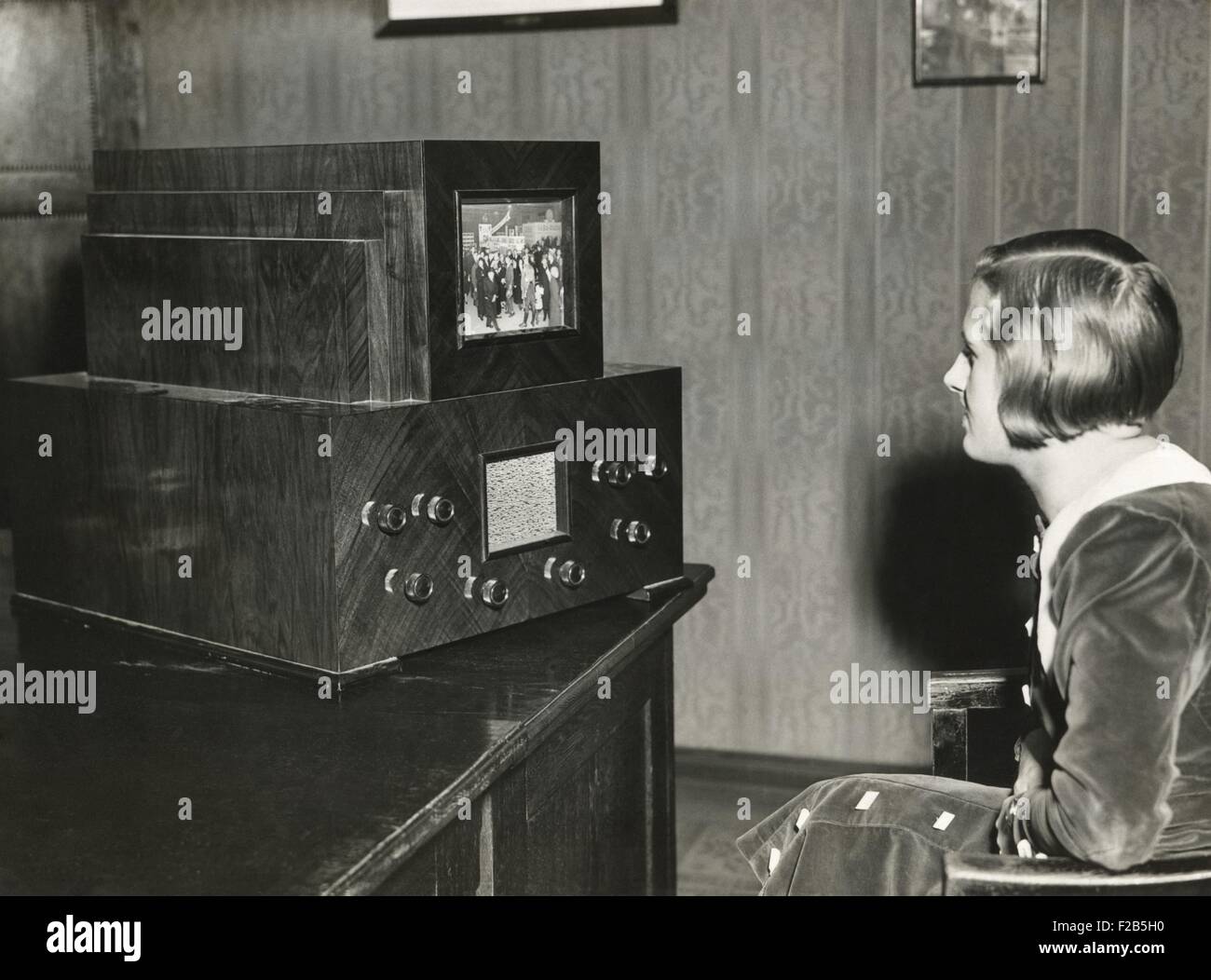 Woman watching a German television with a 14 x 18 centimeter screen. Transmission of live events was still not possible. Instead, events were filmed with moving images and these are broadcast at 25 pictures per second from a special station which possesses the necessary intense lighting. Ca. 1930. - (BSLOC 2014 17 131) Stock Photo