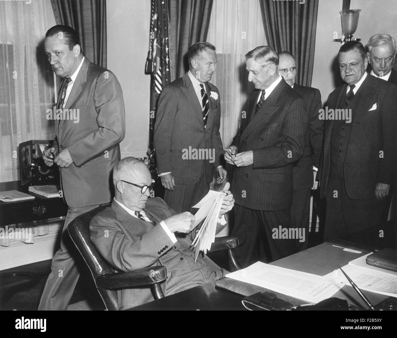 President Eisenhower reads the Highway Act of 1954 before signing. May 6, 1954. Eisenhower saw the German advantage that resulted from the autobahn highway network during World War 2. Standing, L-R: Sen. William F. Knowland; Gen. Wilton Persons; Rep. George Dondero; Rep. Clifford Davis; Sen. Francis Case; Sen. Edward Martin. - (BSLOC 2014 16 230) Stock Photo