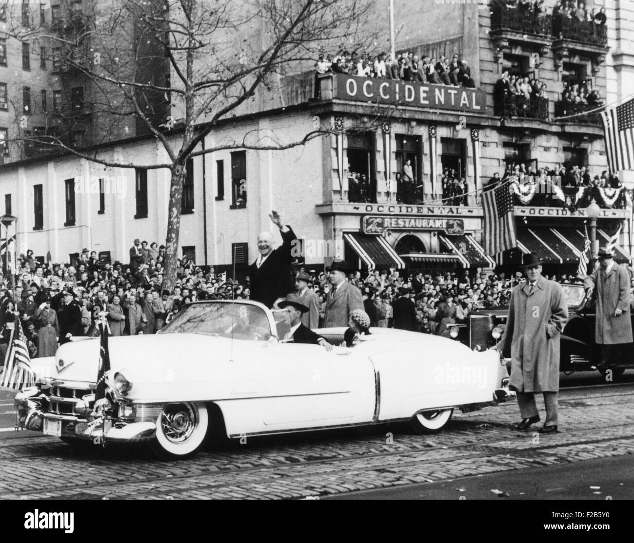 Newly inaugurated President Dwight Eisenhower waves to crowds from an open car. First Lady Mamie Eisenhower sits in the Cadillac limousine, which is escorted by Secret Service guards. - (BSLOC 2014 16 23) Stock Photo