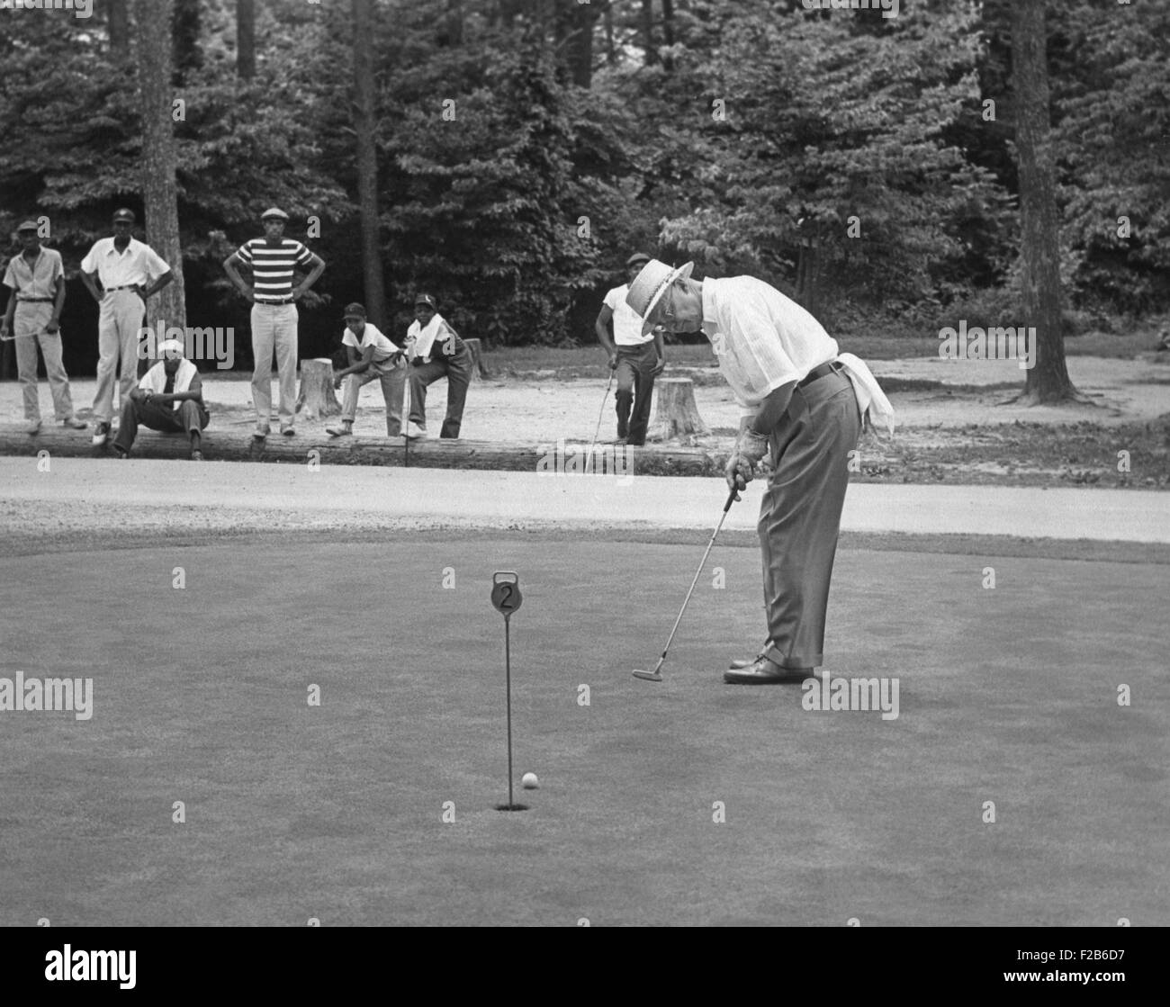 President Dwight Eisenhower on a putting green of a golf course. August 1957. African American caddies watch from the distance. Stock Photo