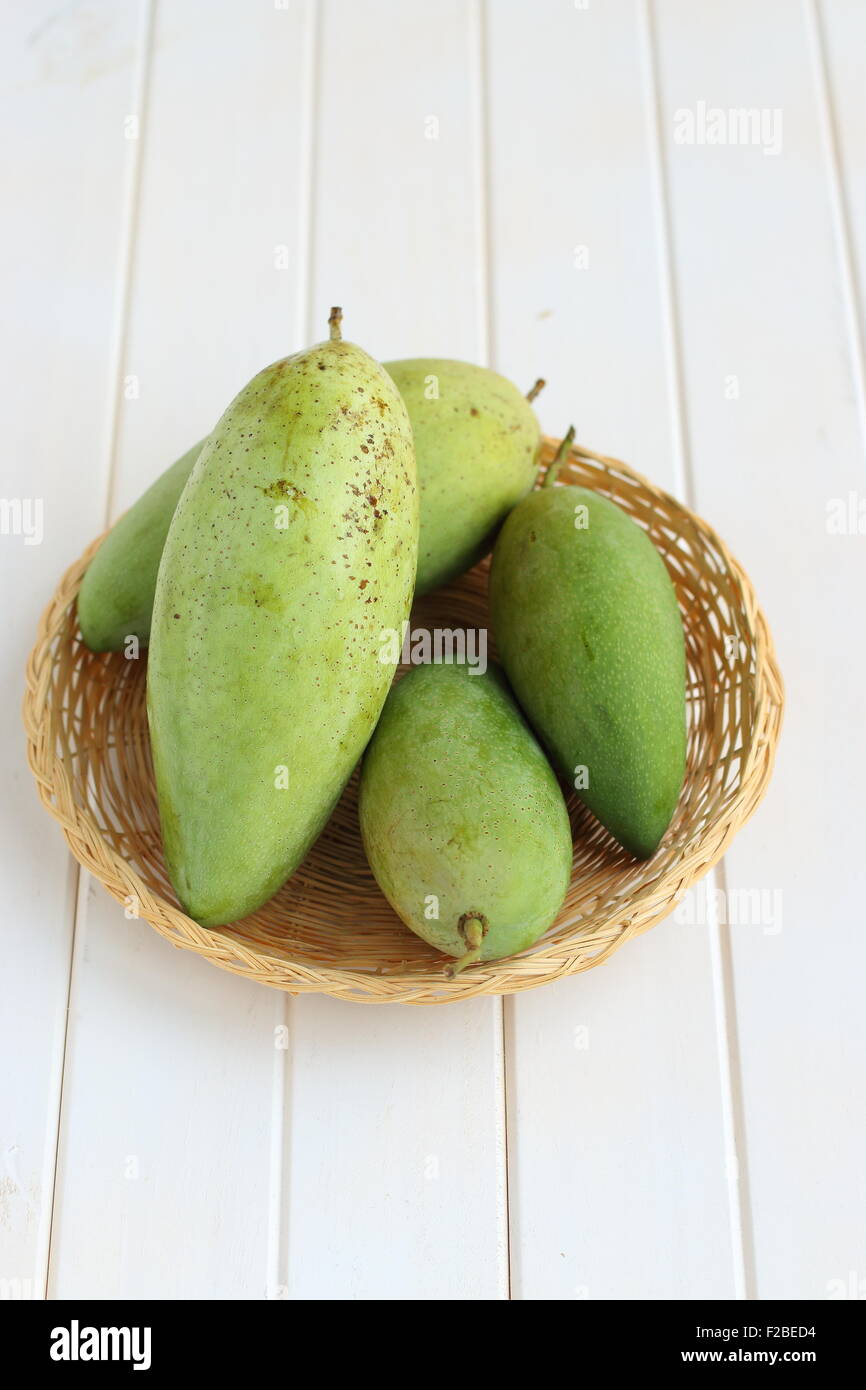 Green mangoes in bamboo basket on white timber Stock Photo
