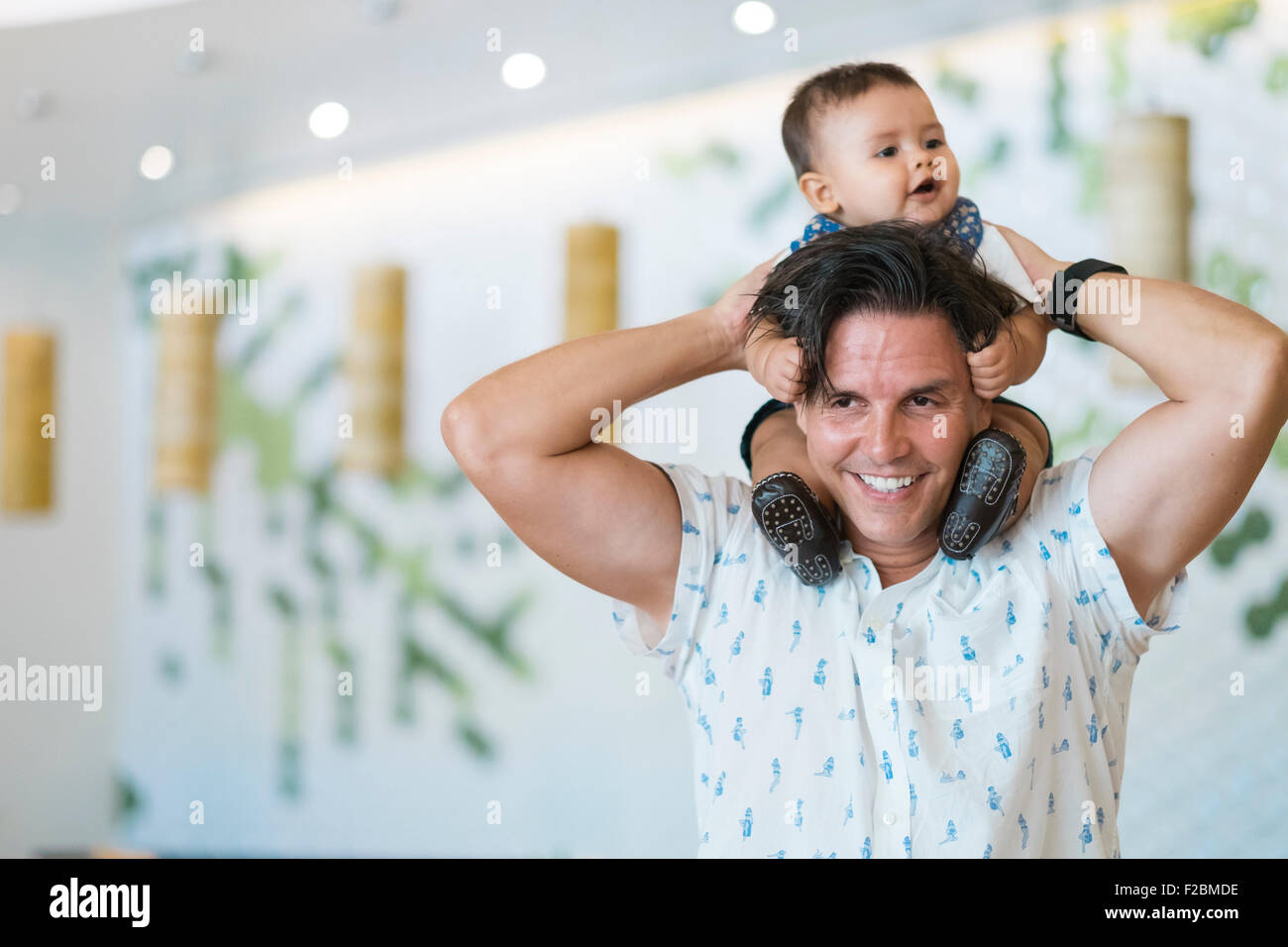 Smiling man is carrying a baby on his shoulders Stock Photo