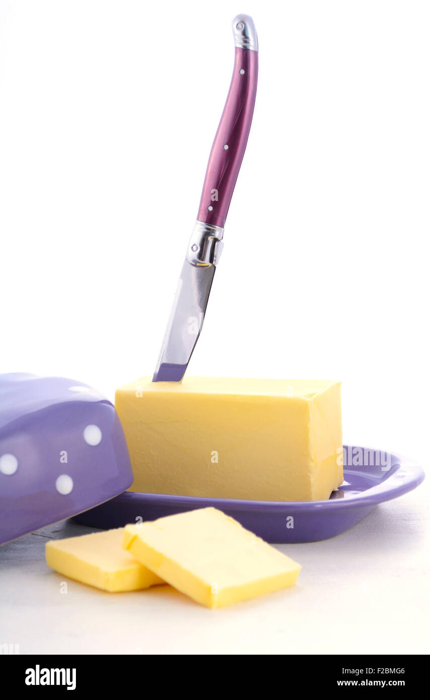 Butter in purple polka dot butter dish and knife on white wood table