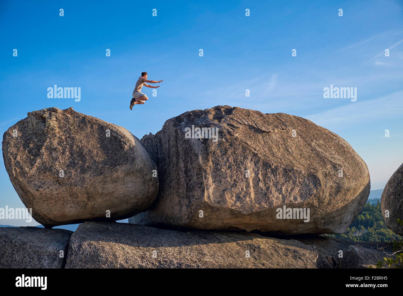 Teenage boy in a remote location in Northern California jumping from one large boulder to another one. Stock Photo