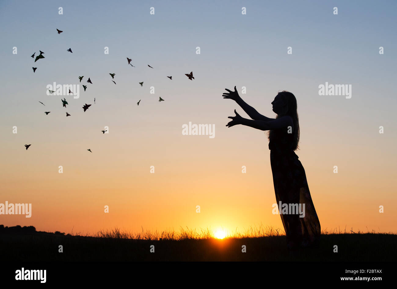 Teenage girl throwing origami butterflies in the air at sunset. Silhouette Stock Photo