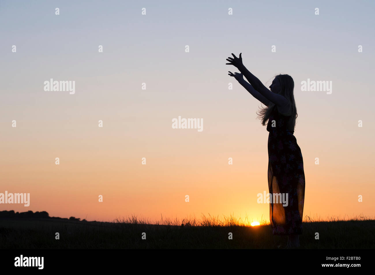Teenage Girl with her arms in the air at sunset. Silhouette Stock Photo