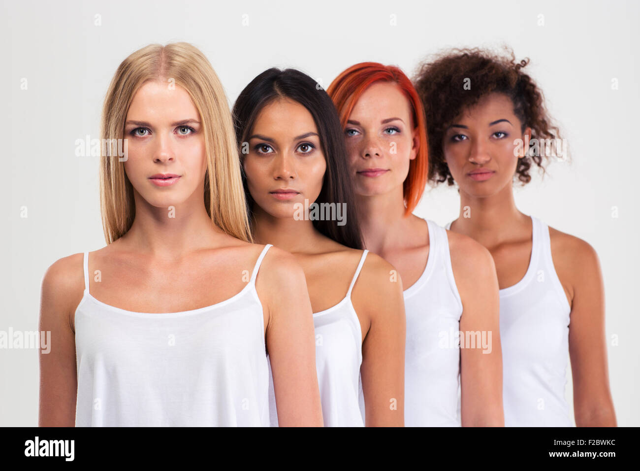 Portrait of a four serious multi ethnic women standing in a row isolated on a white background and looking at camera Stock Photo