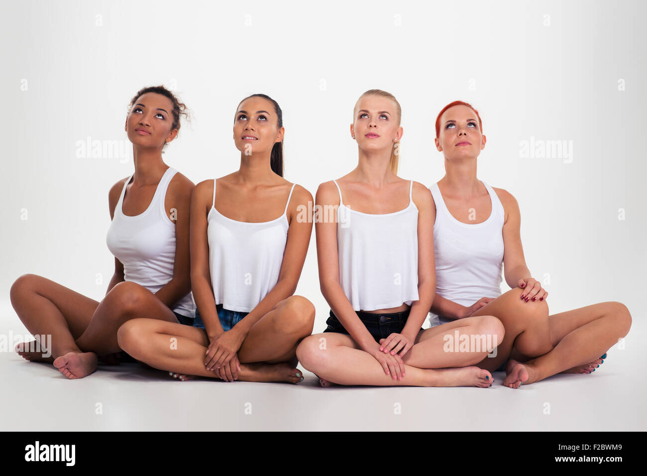 Portrait of a four multi ethnic women sitting on the floor isolated on a white background and looking up at copyspace Stock Photo