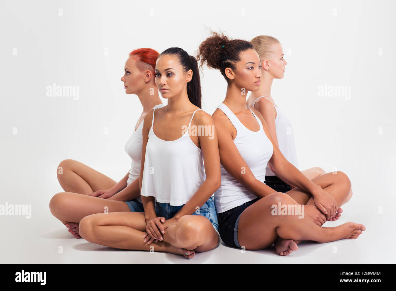 Portrait of a four multi etchnic girls sitting on the floor back to back isolated on a white background Stock Photo