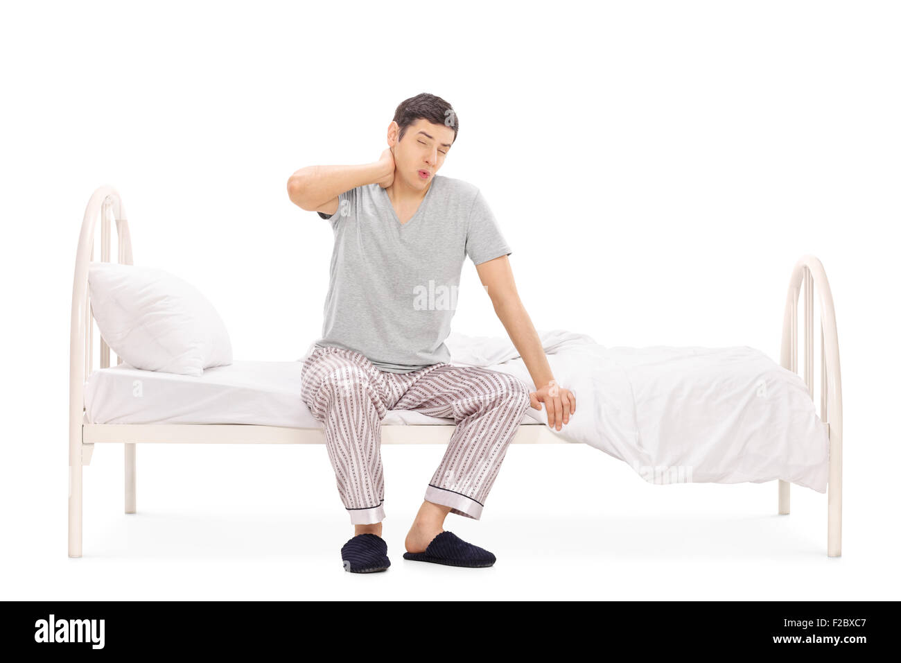 Studio shot of a young man in pajamas waking up with a neck pain isolated on white background Stock Photo