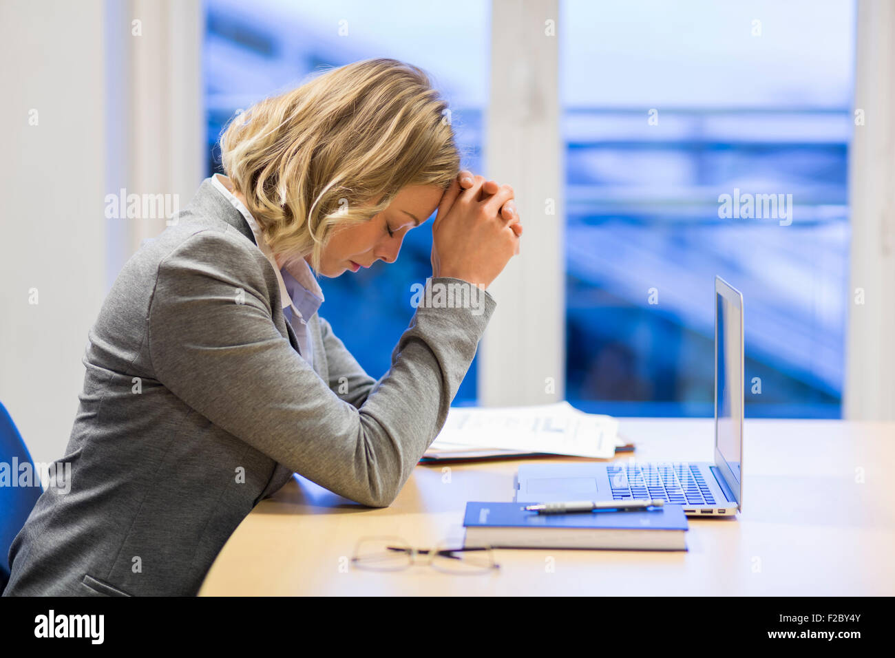 pensive business woman sitting in office, hands on forehead Stock Photo