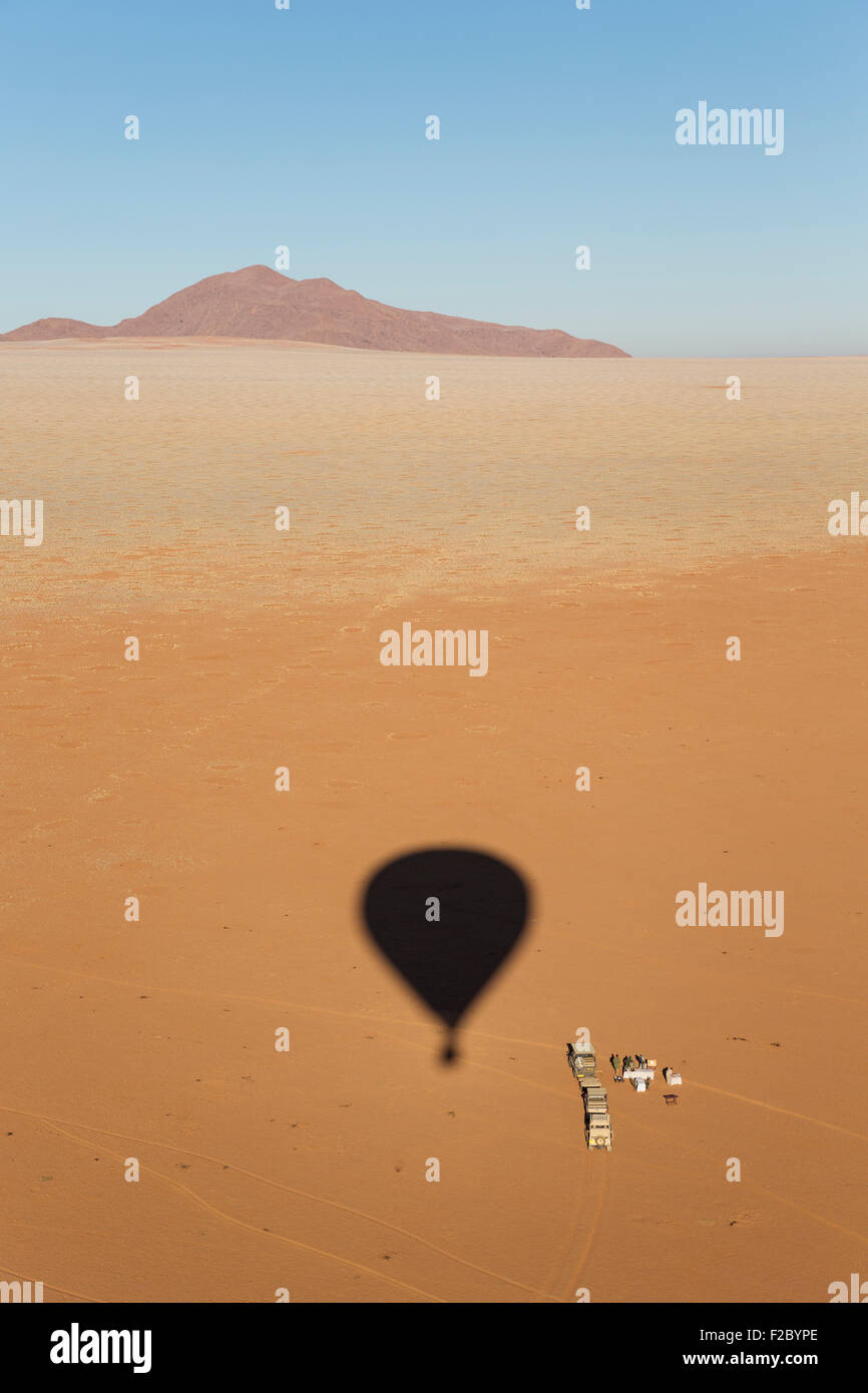 Shadow of a hot-air balloon at the intended landing spot in a true desert environment, ground crew prepares an opulent Stock Photo