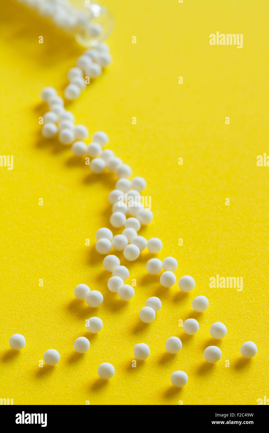 Closeup view of homeopathic pills (made from inert substance - sugar/lactose) spillage effect from a bottle on a yellow surface. Stock Photo