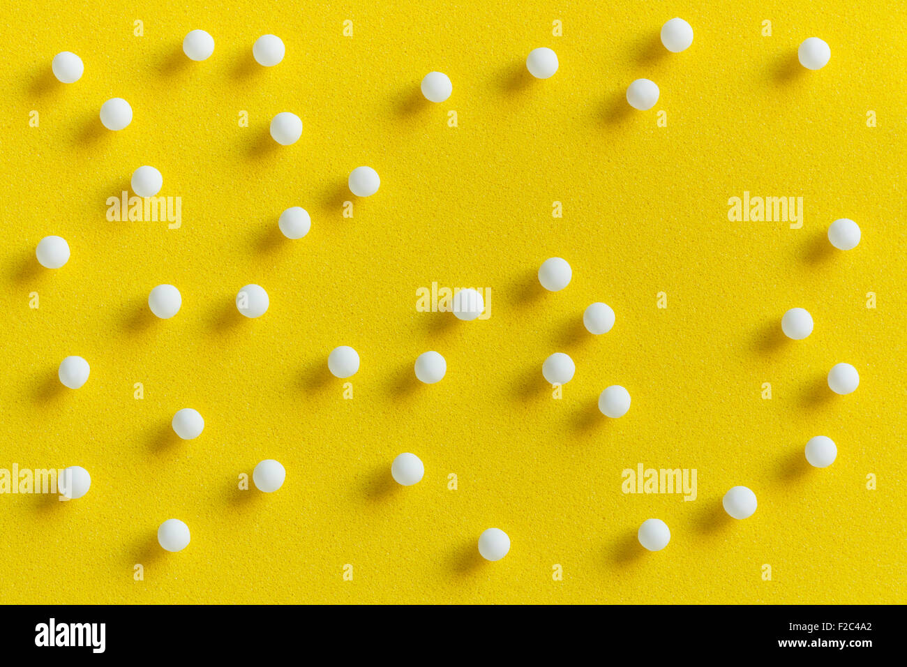 Overhead view of homeopathic pills (made from inert substance - sugar/lactose) scattered on a yellow surface. Stock Photo