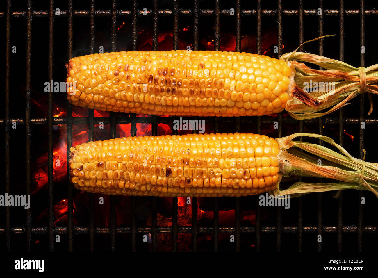 Whole Sweet Corn with leaves grilled on hot coal fire. Seen from above Stock Photo