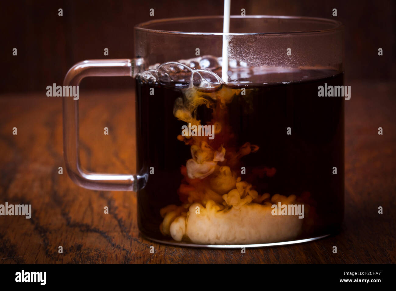 The process of brewing tea, pouring hot water from the kettle into the Cup,  steam coming out of the mug, water droplets on the glass, black background  Stock Photo