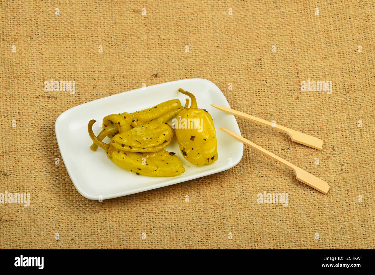 Mediterranean snack of four pickled green pepper in white plate with two skewers on burlap jute canvas Stock Photo