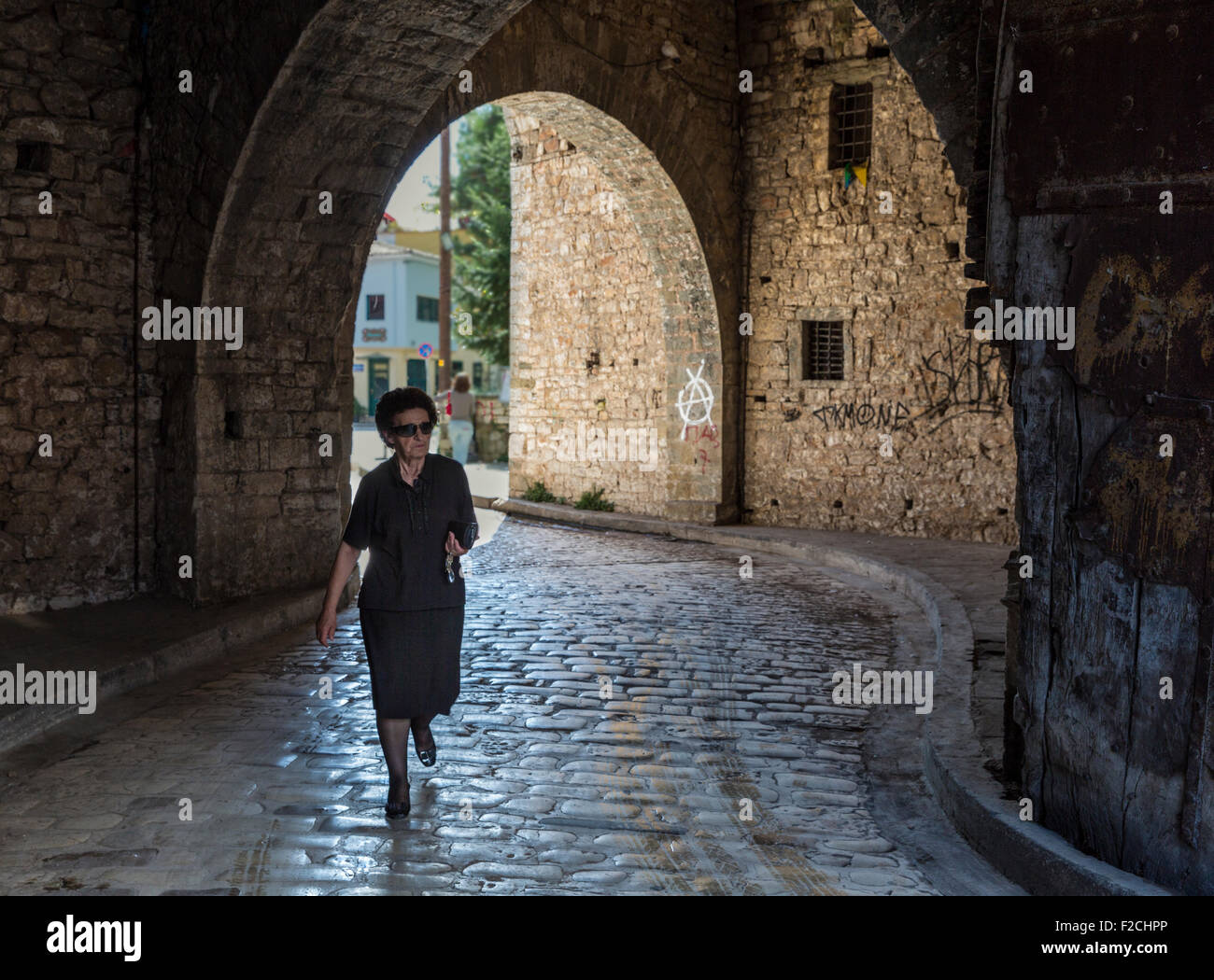 Greek woman in black dress exiting the old city of Ioannina via an arched passageway in the city walls Stock Photo