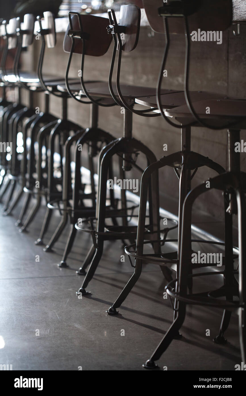 old metal bar chairs lined up at  bar, backlit Stock Photo