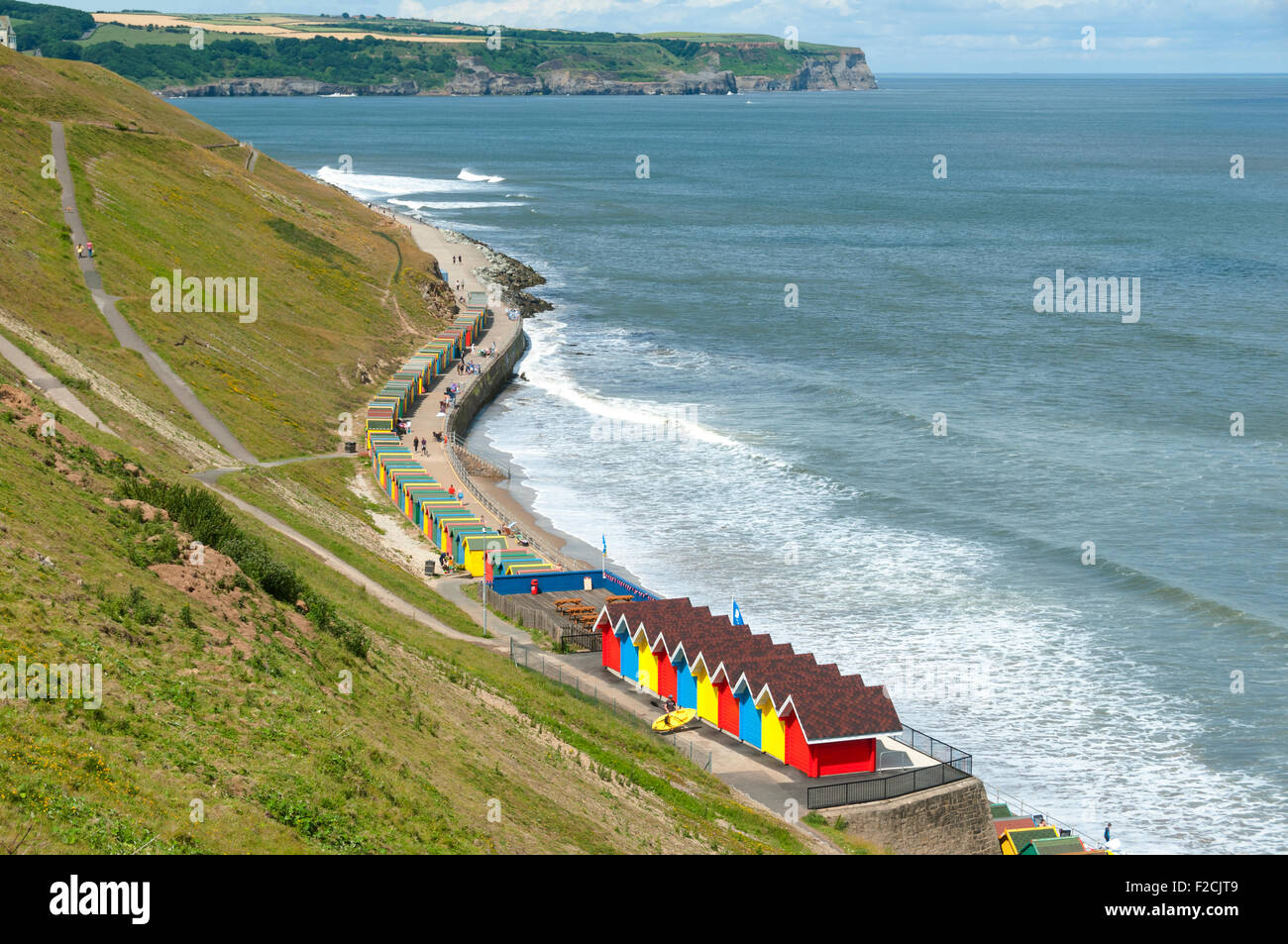 Multi-coloured beach huts at Whitby Beach, Whitby, Yorkshire, England, UK.  Sandsend Ness in the distance. Stock Photo