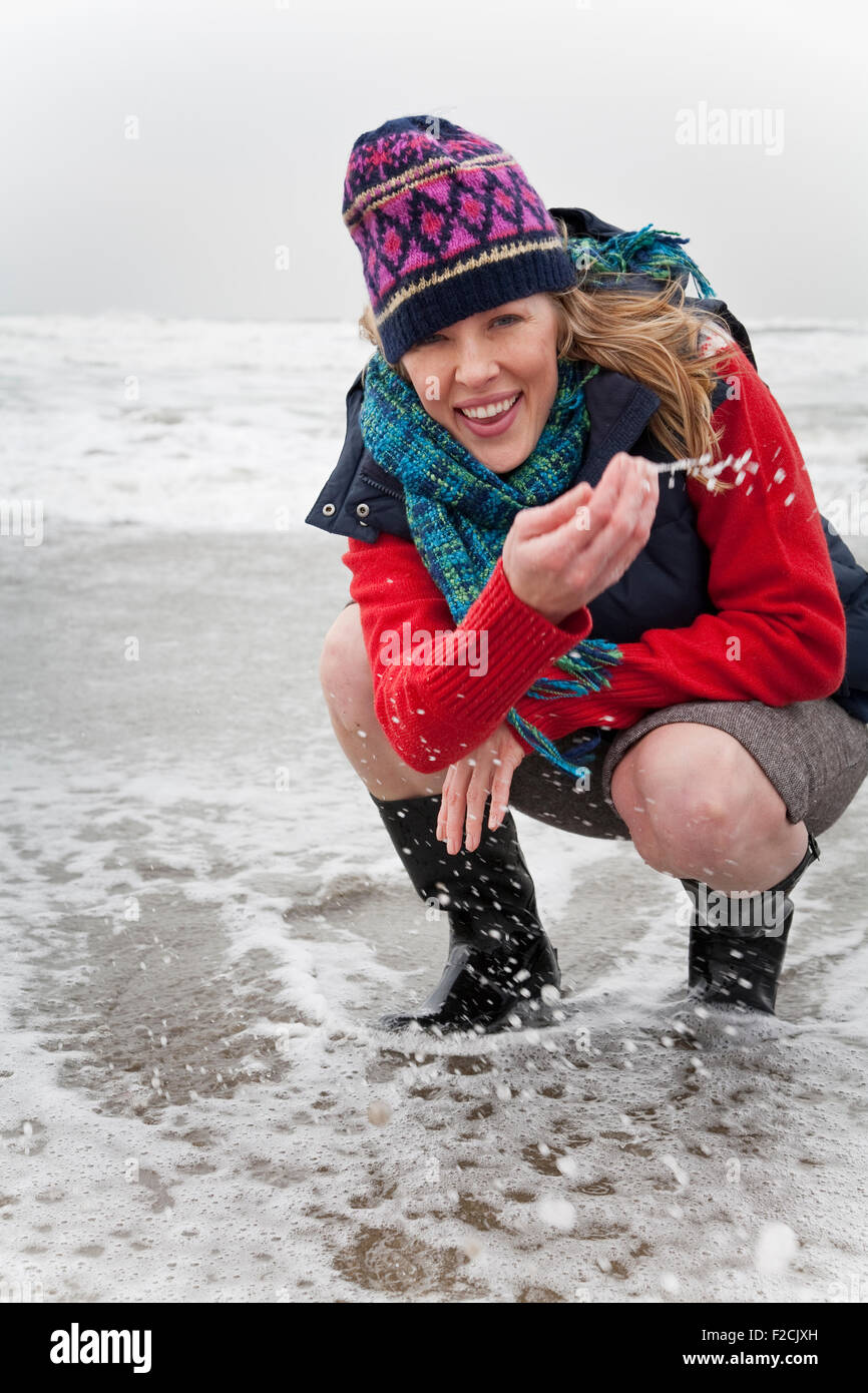 Young woman squats in the ocean wearing winter clothes Stock Photo