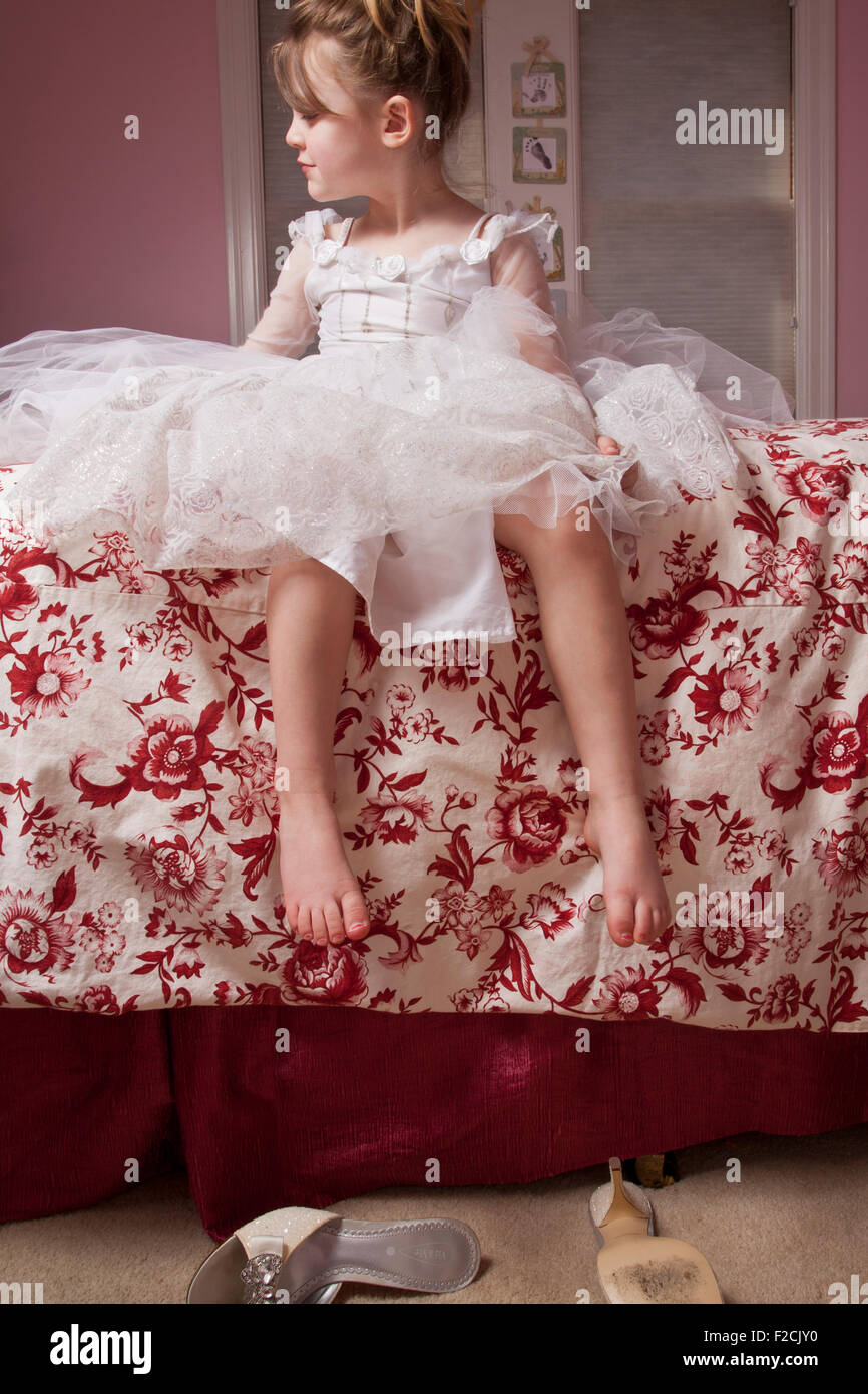 Young girl sits on bed looking to her right in frilly dress Stock Photo