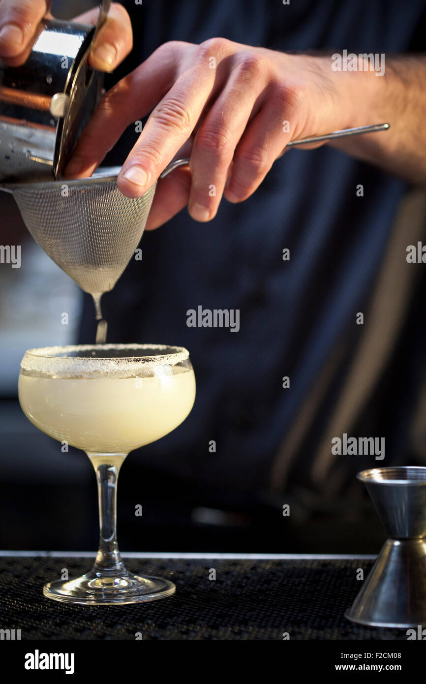Cropped and unidentified bartender pours a cocktail through a strainer Stock Photo