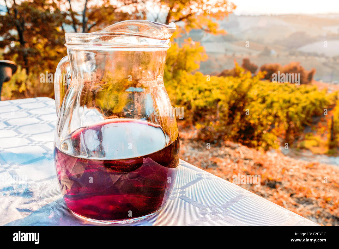 jug of genuine and non-industrial wine on a table with vineyards, farmlands and green vegetation of the countryside in the background Stock Photo