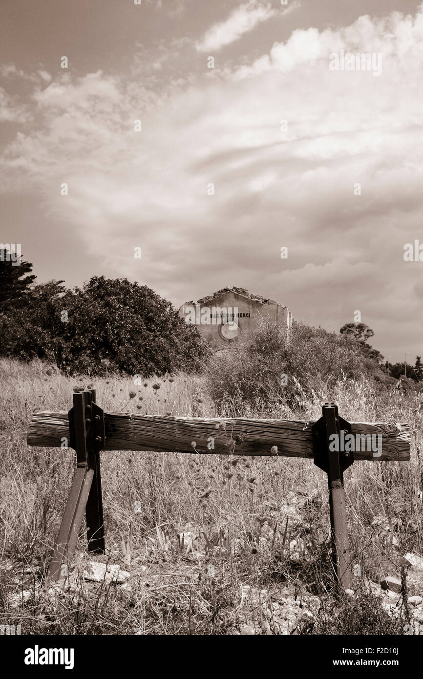 Black and white sepia tinted photograph of overgrown disused railway station with buffer stop in the foreground in Sicily Italy Stock Photo