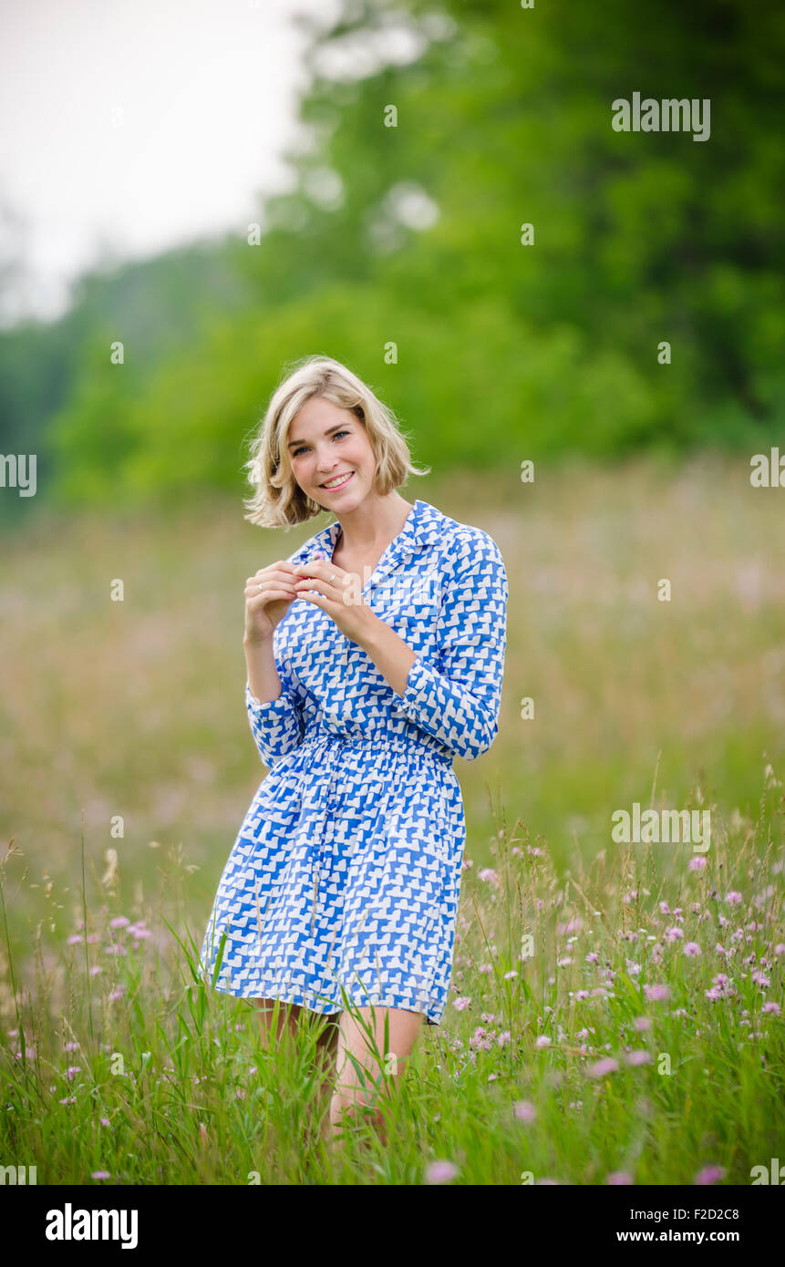 Beautiful Teenage Girl Stands in Field Wearing a Blue Dress with Green Trees in Background Stock Photo