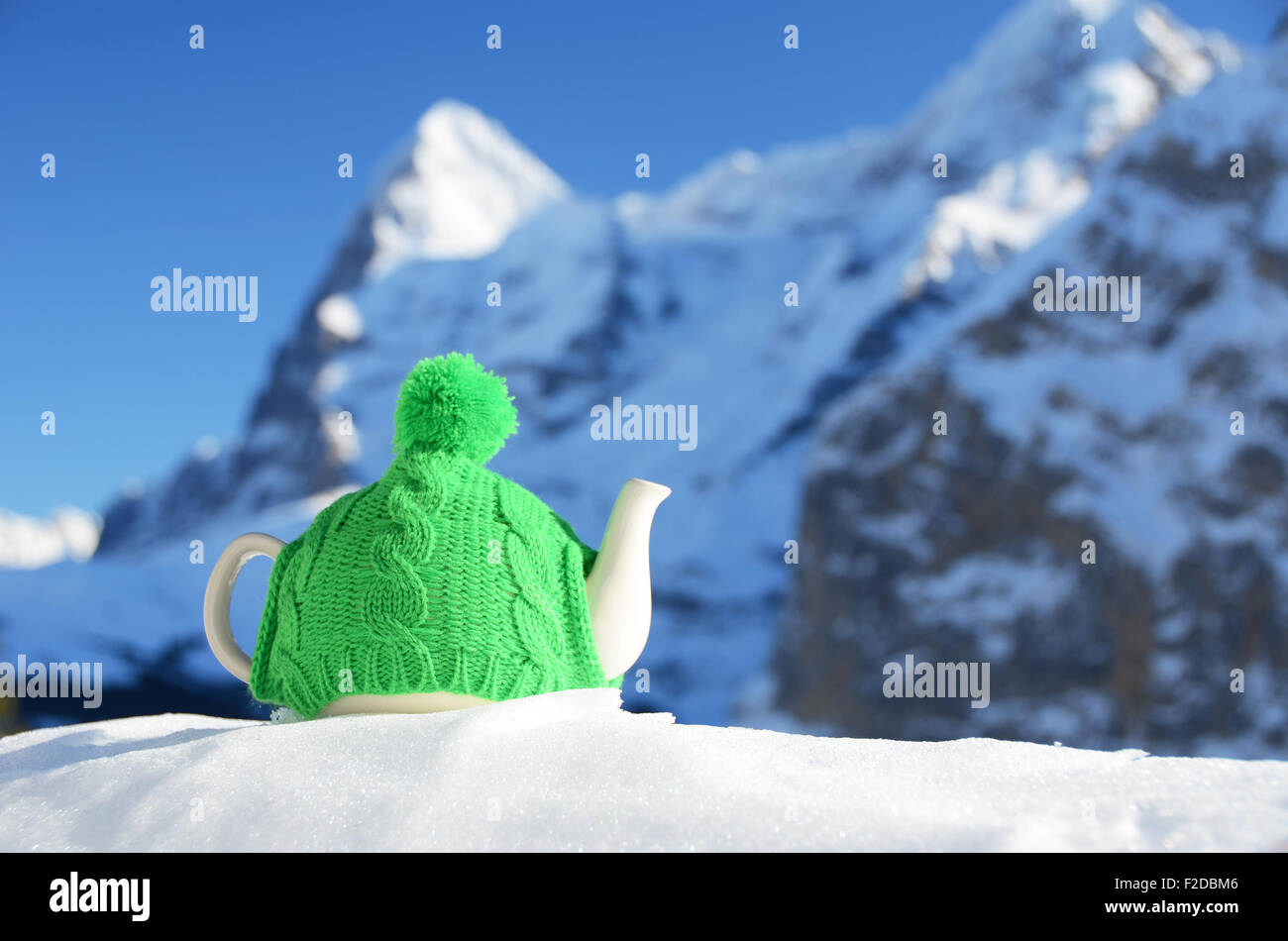 Tea pot in the knitted cap on the snow against mountain peak Stock Photo
