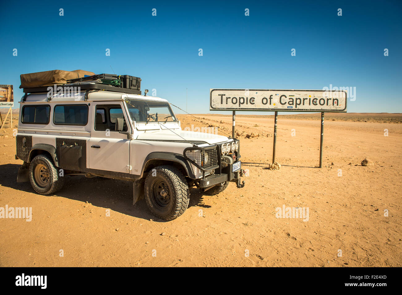 Land Rover Defender 110  parked in the desert next to a sign for the Tropic of Capricorn in Namibia, Africa Stock Photo