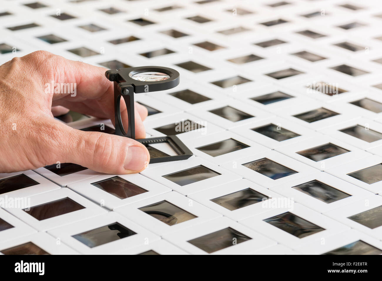 series of photo slides on a table with hand holding loupe Stock Photo