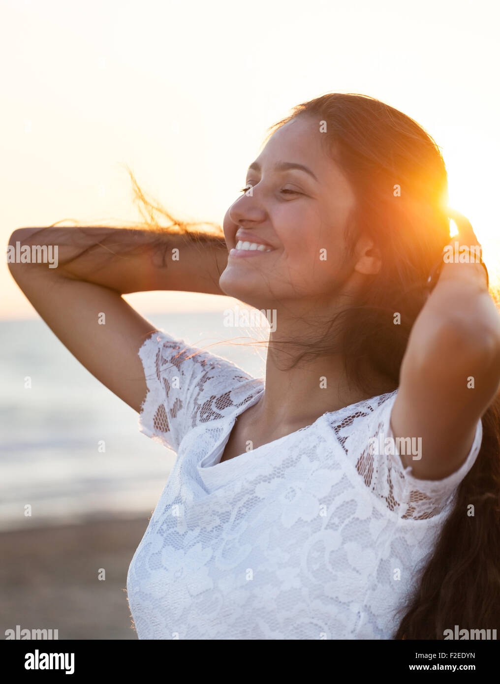 Beautiful young teenager with a white dress on the beach at sunset. Stock Photo