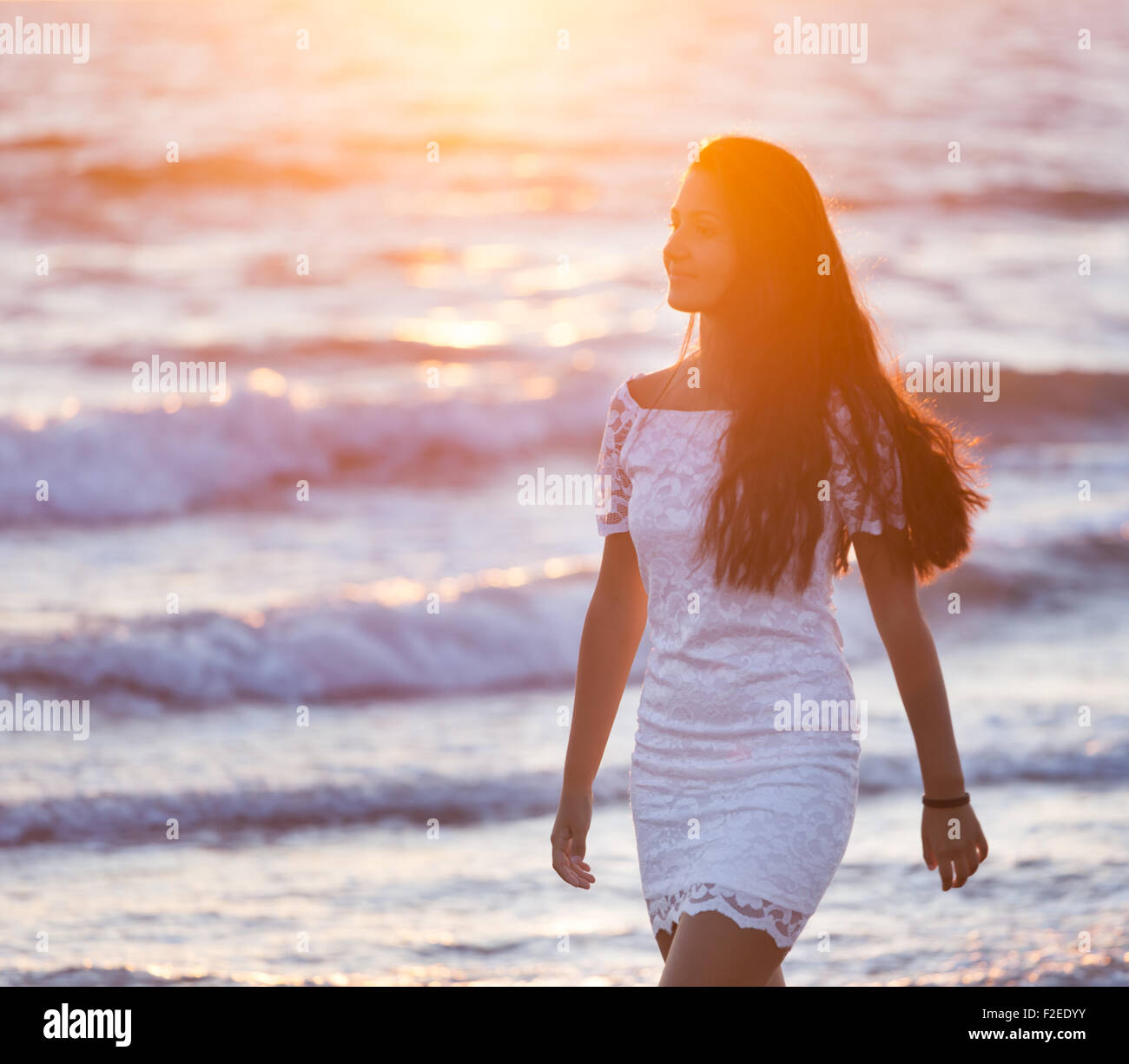 Beautiful young teenager with a white dress on the beach at sunset. Stock Photo
