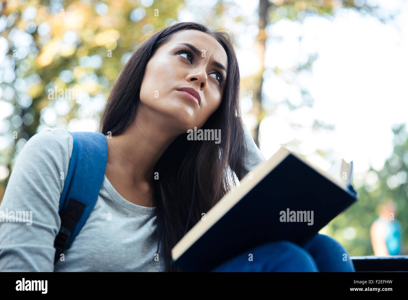 Portrait of a pensive female student holding book and looking away ...