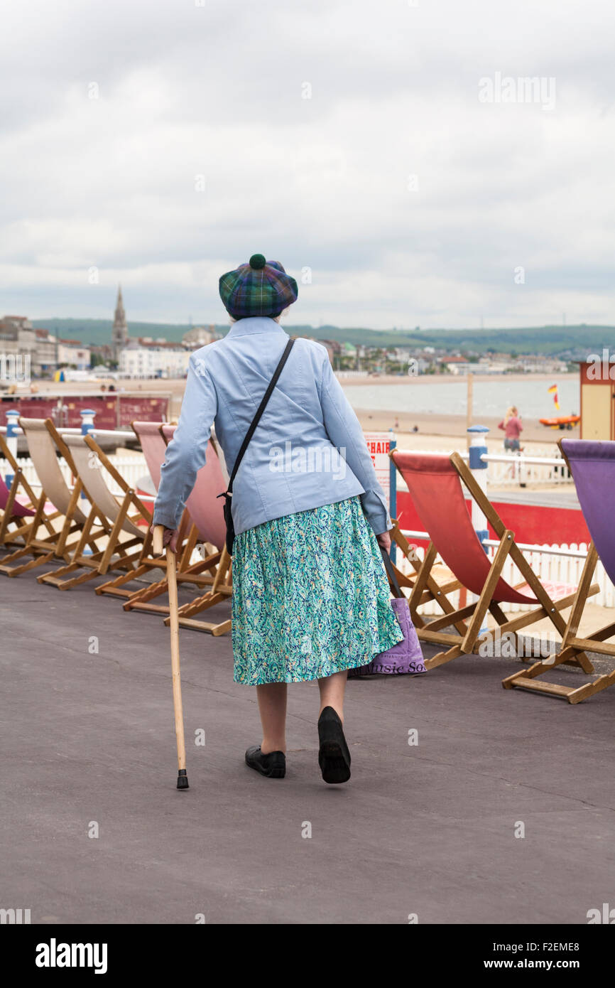 Rear view of elderly walking with walking stick along Weymouth ...