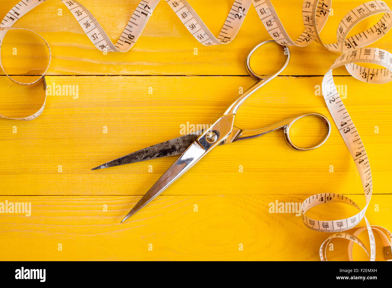 Metal scissors and measure tape on yellow background. Fashion industry concept. Stock Photo
