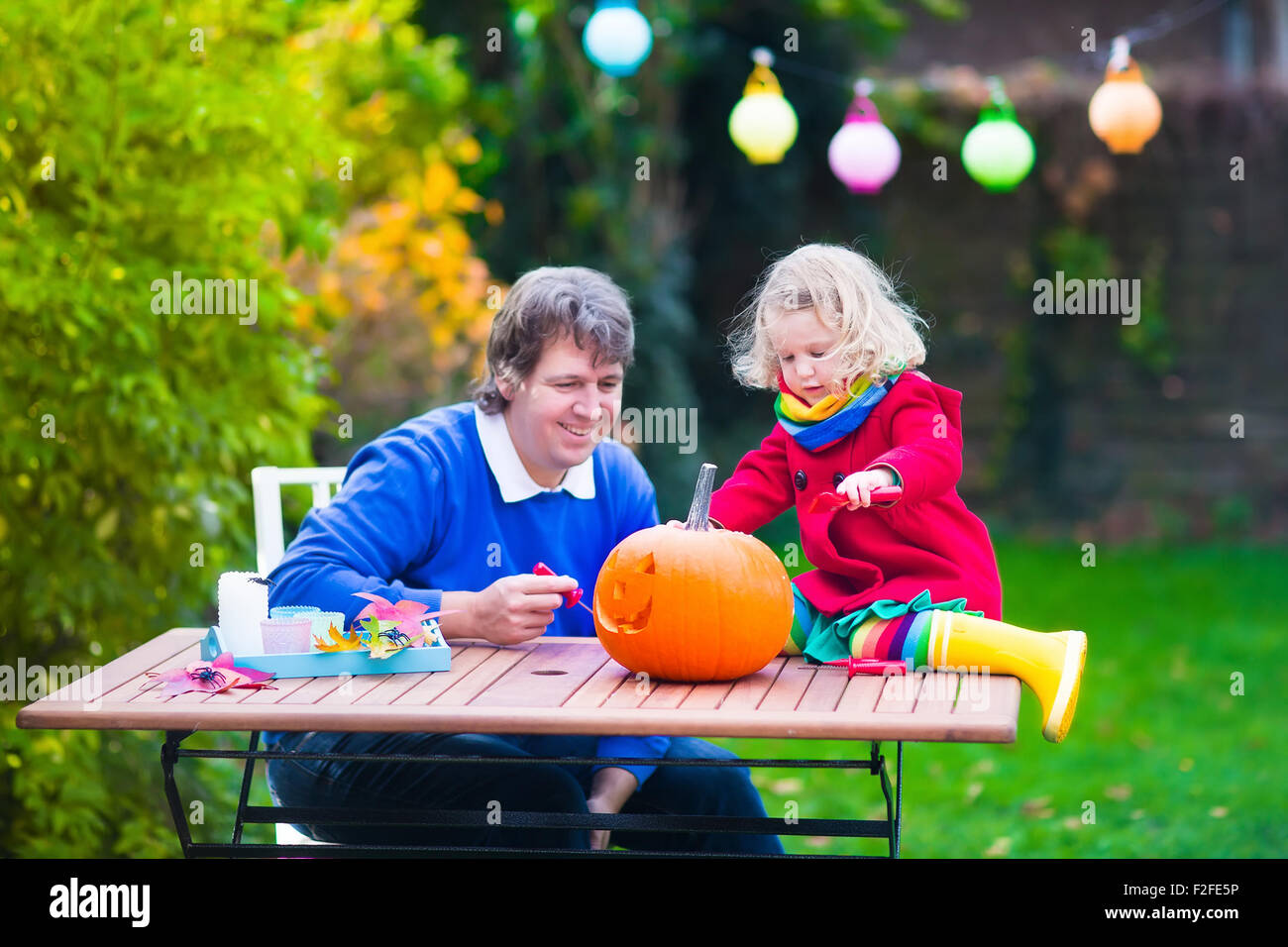 Family carving pumpkin at Halloween. Dressed up child trick or treating. Kids and parents trick or treat. Child in witch costume Stock Photo