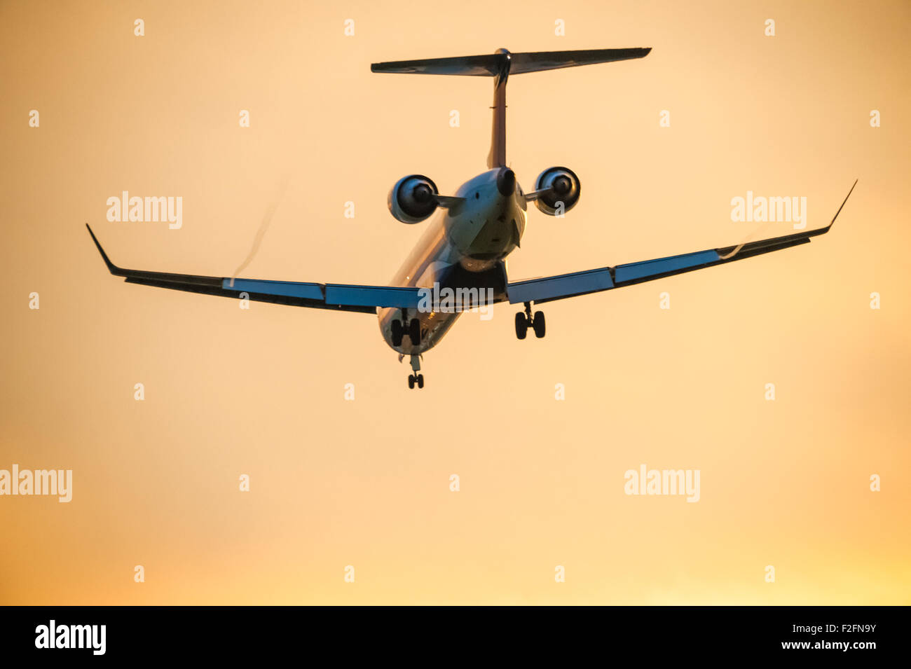 Airline passenger jet descends for landing under an orange sunset sky. Stock Photo