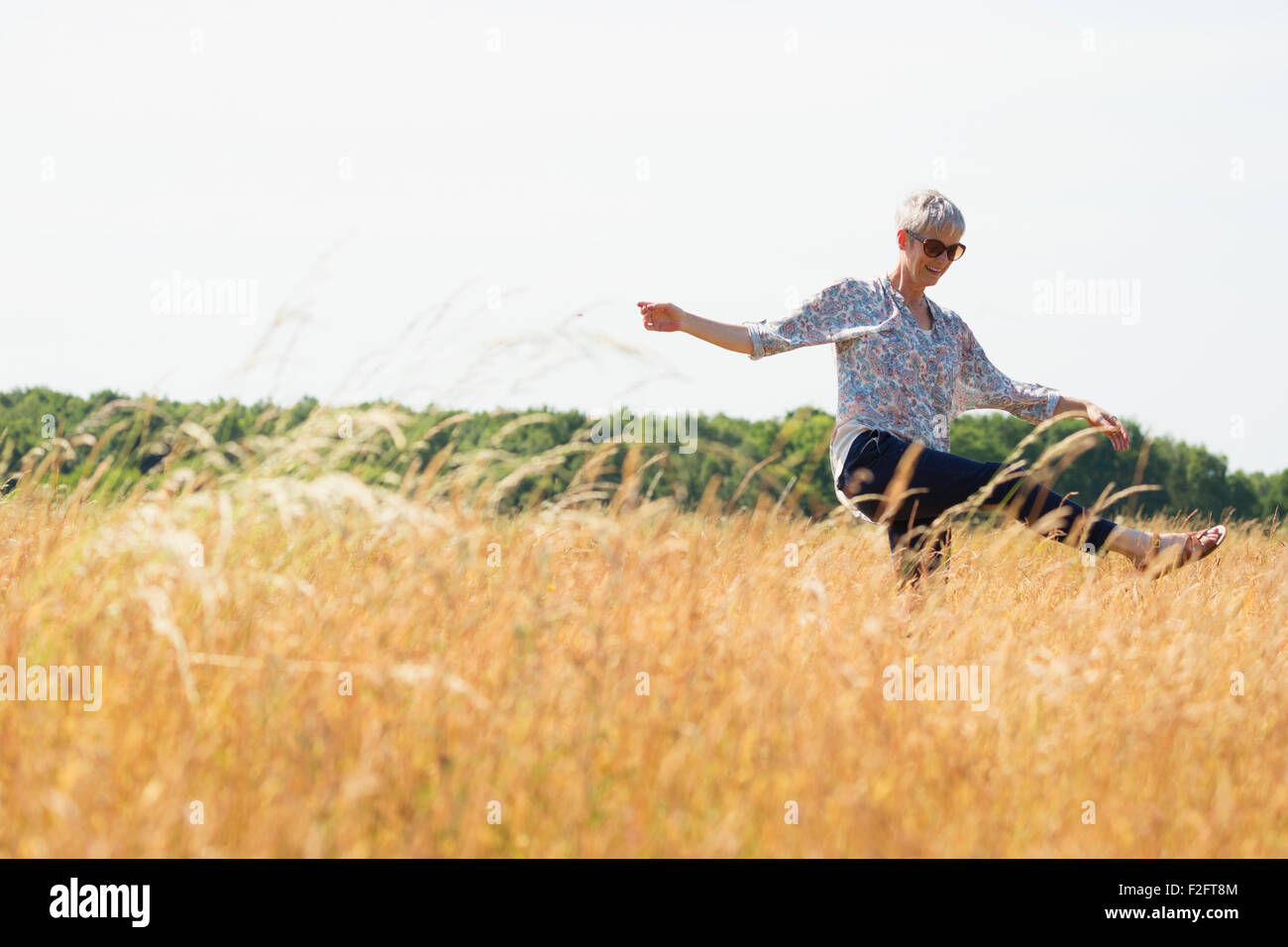 Playful senior woman dancing in sunny rural field Stock Photo