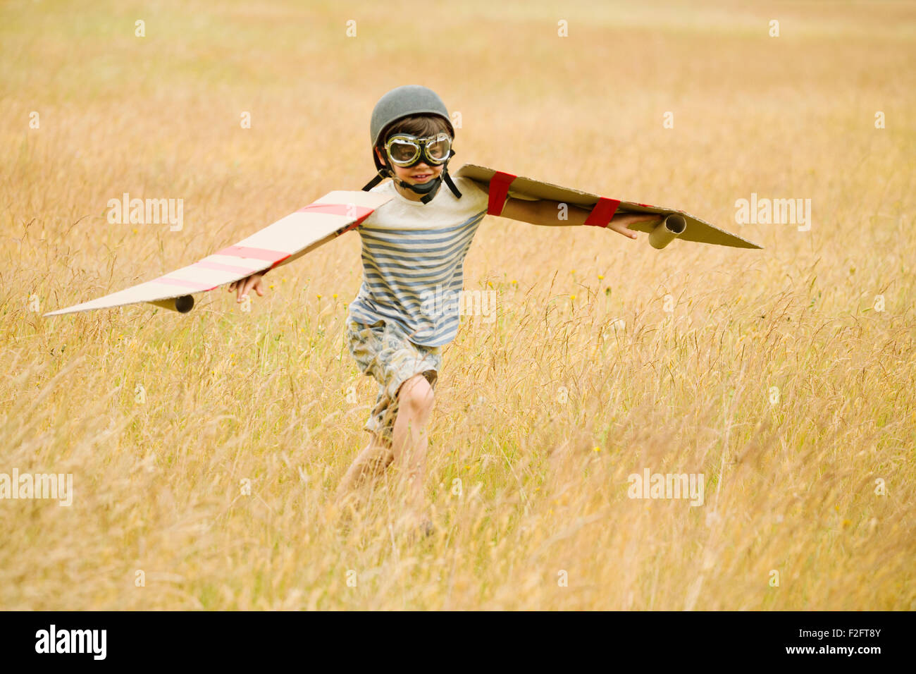 Boy running with wings and aviator’s cap and flying goggles in field Stock Photo