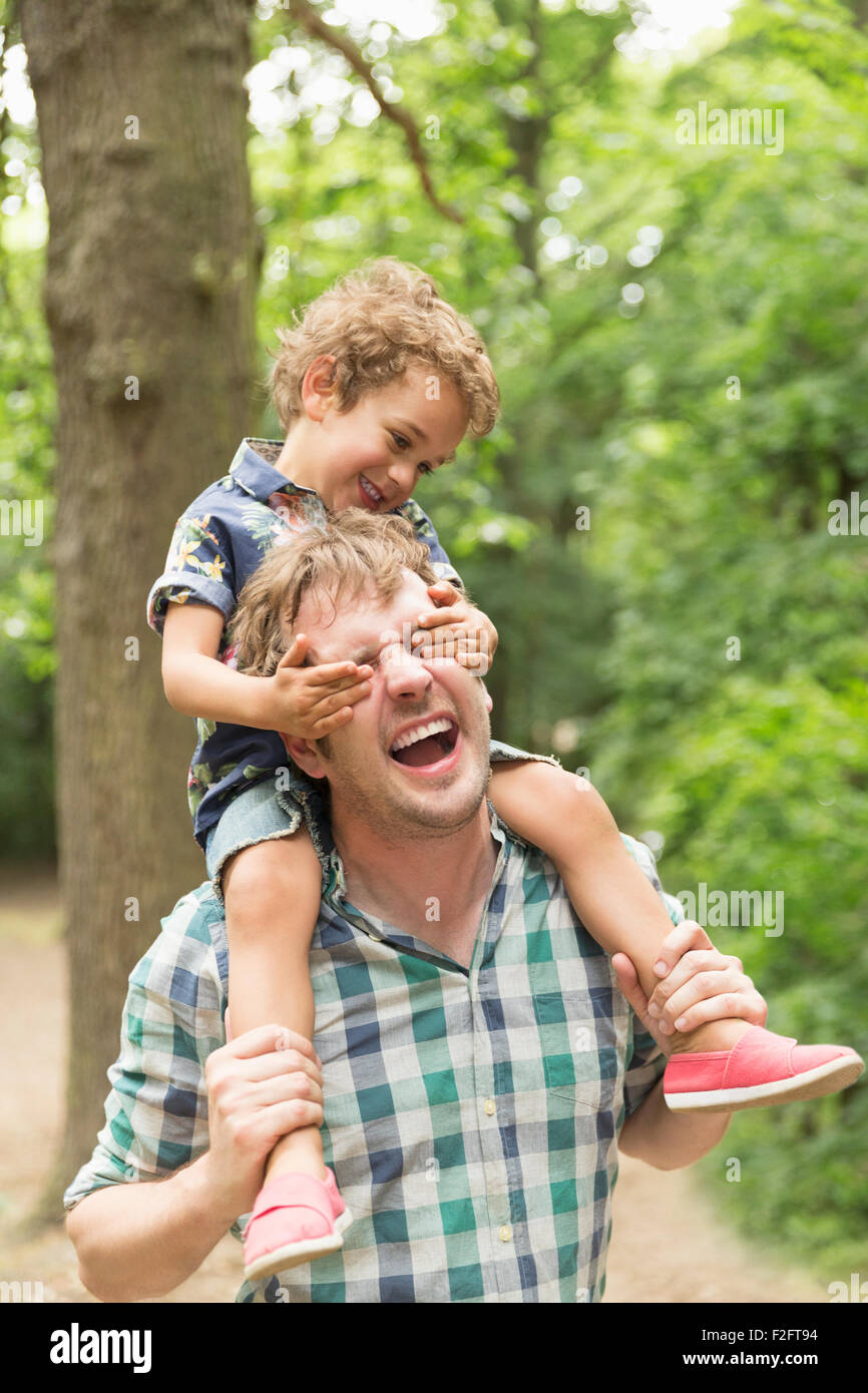 Playful son covering father’s eyes in woods Stock Photo